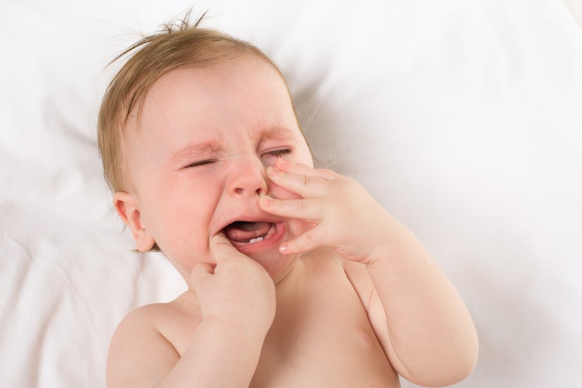 A baby is crying with its index finger inside the mouth.