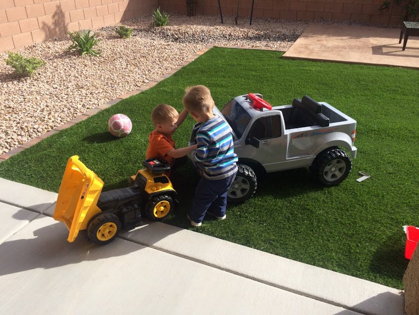 Two boys playing with big car toys in a garden