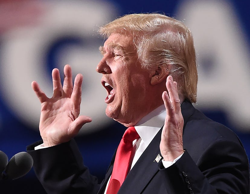 Donald Trump giving a speech in front of the microphone with his hands up.