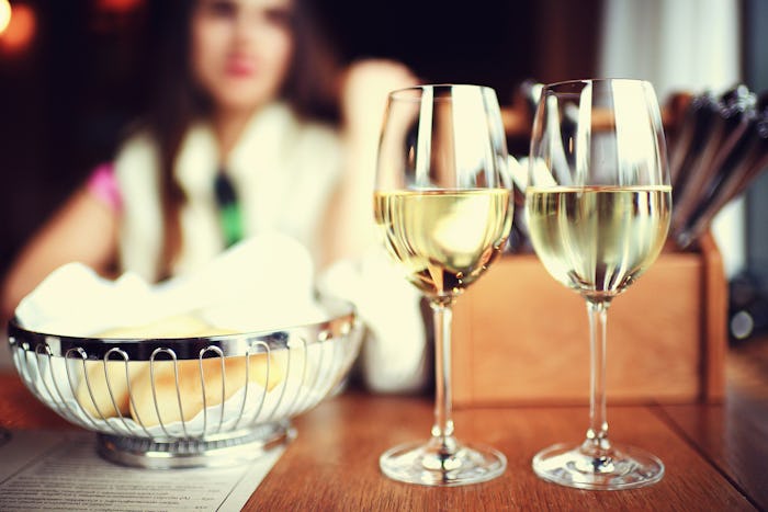 Two wine glasses on a table, a bread basket and a blurred out woman in the background