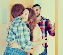 A woman hugging her mother in law while her husband is standing behind her
