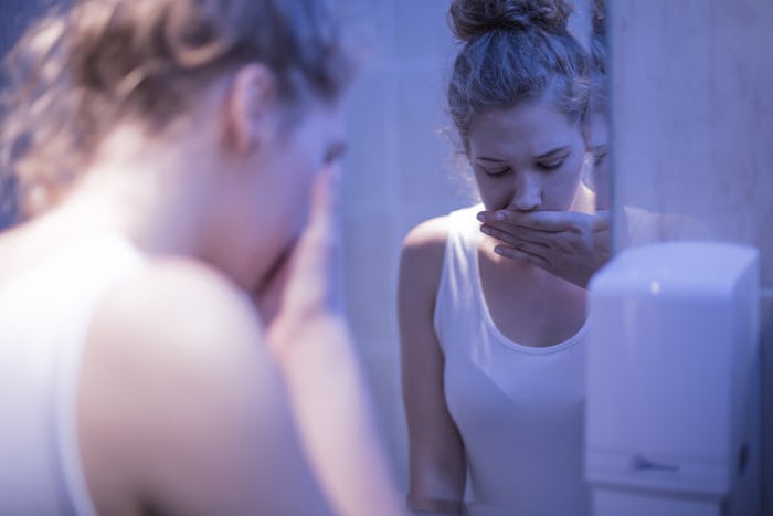 Mother recovering from an eating disorder standing in front of the mirror covering her mouth with he...