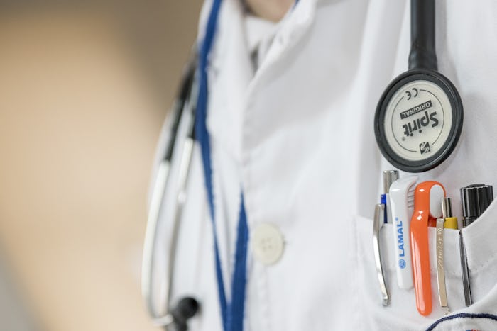 A close up of a doctor wearing a stethoscope around his neck and having a lot of pens in his scrub p...