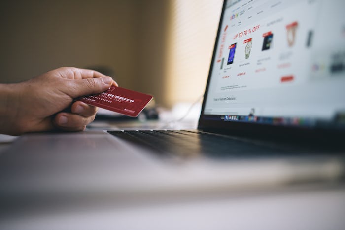 A woman holding a red debit card next to her laptop as she is shopping during Cyber Monday from the ...