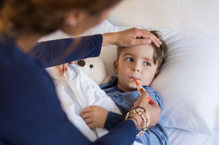 A little boy in bed getting his temperature measured by his mom