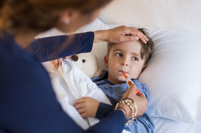 A little boy in bed getting his temperature measured by his mom 