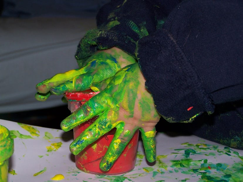 The kid's hands covered in green paint, playing with the red container.