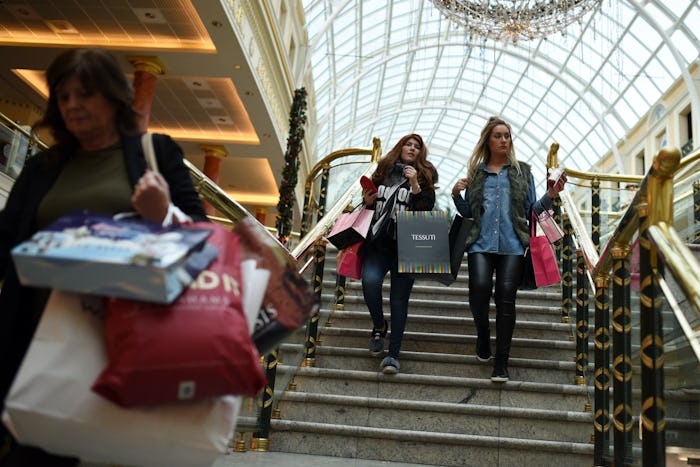 Two young women going down the stairs at a mall while carrying shopping bags.