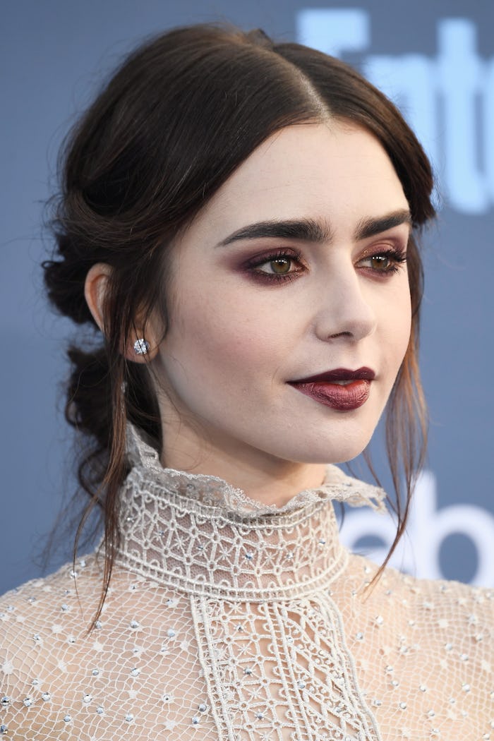 A closeup of Lily Collins at the Golden Globes with an up do, a smoky eye and burgundy lipstick