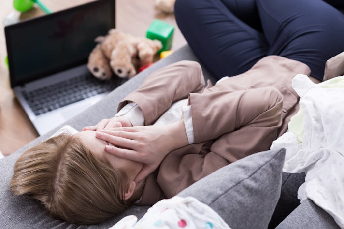 A mom stressed out on the couch with her laptop and kids toys on the side
