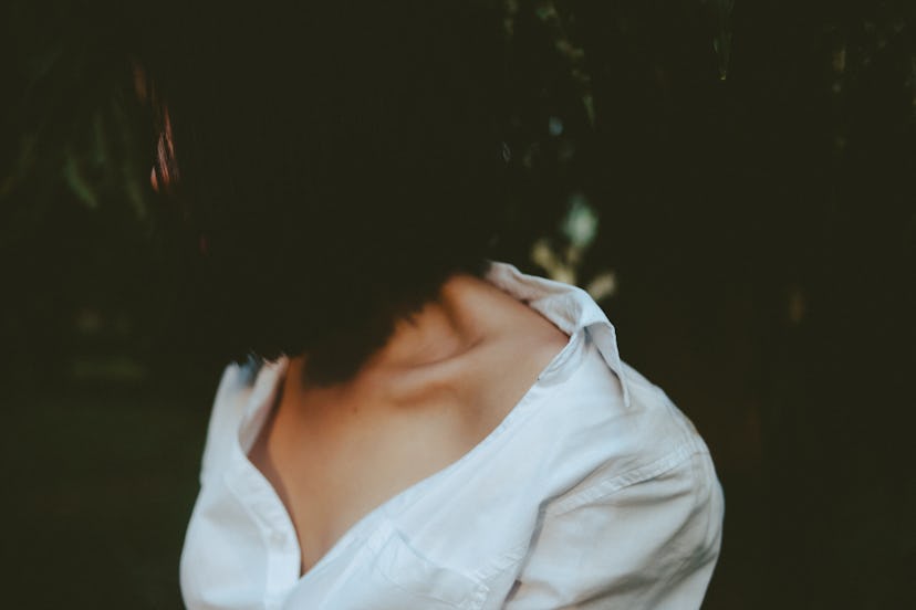 A girl with short black hair covering her face wears a white shirt