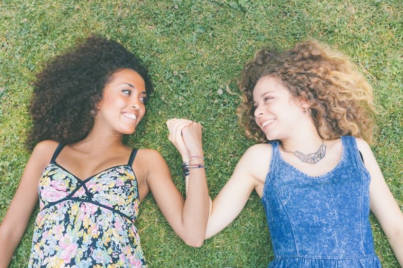 Two girl lying on grass and holding hands