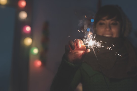 A woman holding a sprinkler at a new years event with multicolored lights behind her