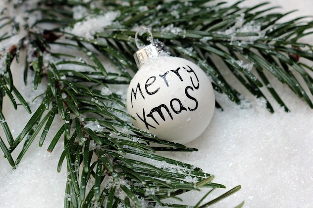 A white Christmas ornament surrounded by snow and a Christmas tree branch
