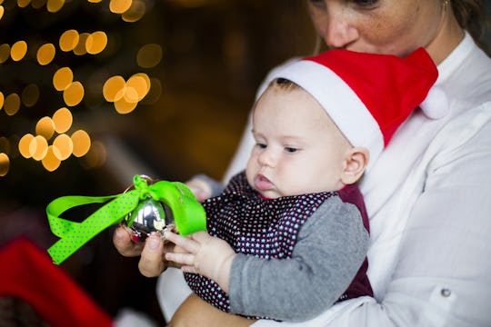 A baby in a christmas hat holding a christmas tree ornament and staring at it intently.