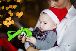 A baby in a christmas hat holding a christmas tree ornament and staring at it intently.