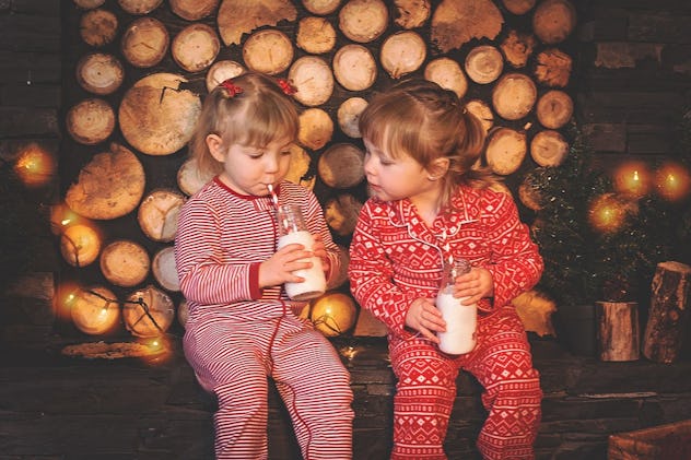 Two small girls drinking milk and wearing Christmas onesies