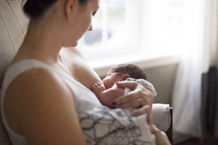A mom breastfeeding her child next to a window in her bedroom