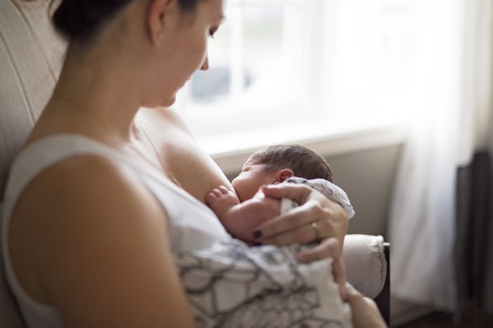 A mom breastfeeding her child next to a window in her bedroom 