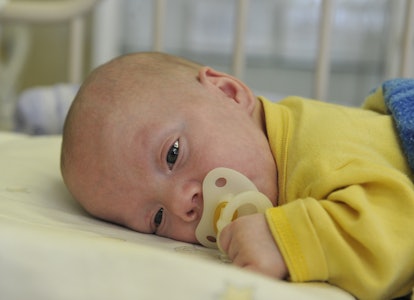 A prematurely born baby lying on its stomach in a yellow sweater and pacifier