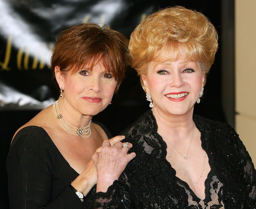 Two older women dressed formally are posing for a picture while holding hands.
