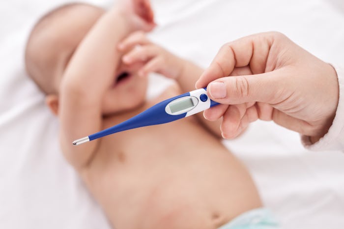 A baby with RSV covers its face with his hands while their temperature is being taken