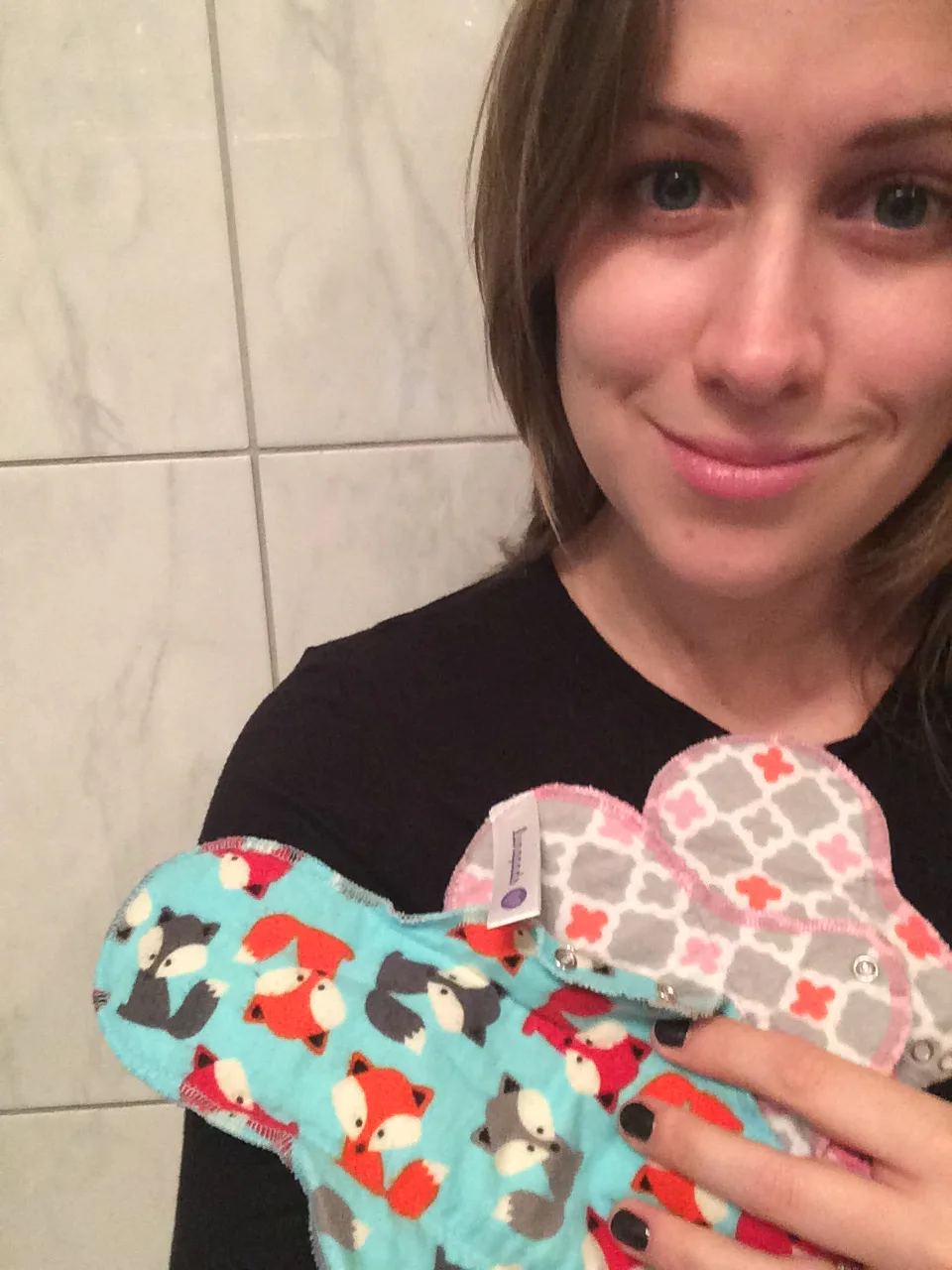 A girl smiling at the camera and holding reusable menstrual pads in different colors