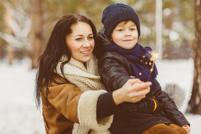 A woman and her kid holding a sparkler outside in the snow