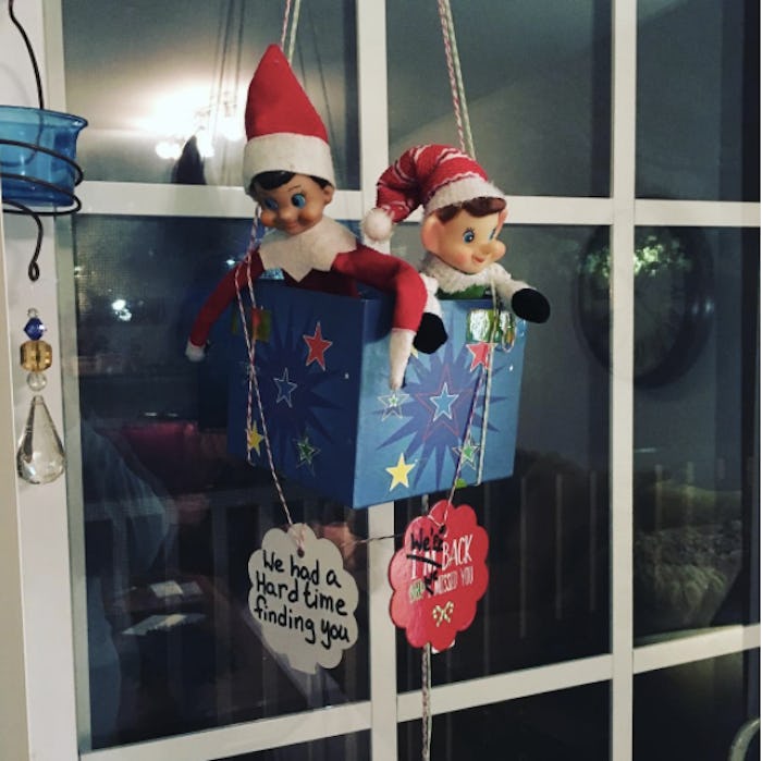 Two elf on the shelf dolls in a blue box hanging on a window