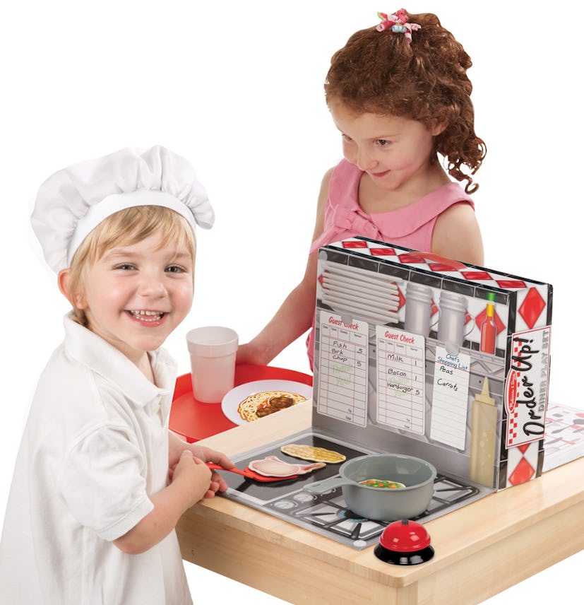 Small girl and boy playing with a dinner play set