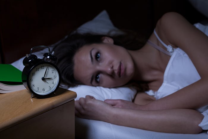 A woman struggling with insomnia looking at her alarm clock while lying in her bed