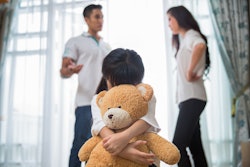 Parents fighting while toddler hugs her teddy bear in front of them