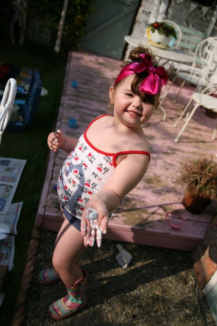 A little girl with a magenta ribbon in her hair posing outside in a tank top and shorts