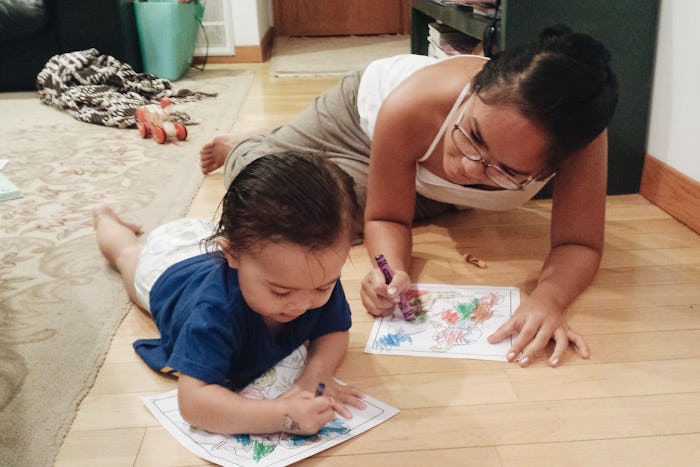 A stay-at-home-mom lying on the floor with her daughter coloring with crayons.