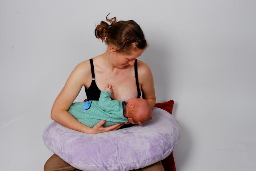 A mother breastfeeding her kid while holding him on the pillow