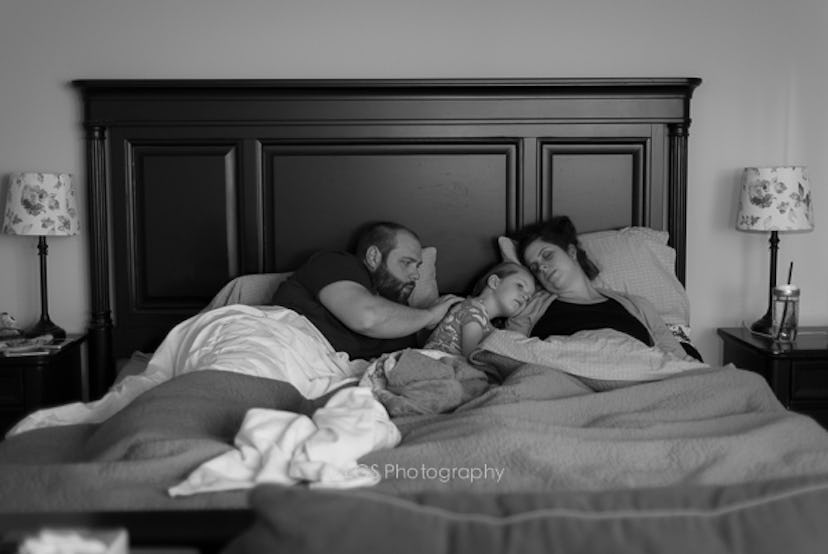 A woman preparing for a home birth lying in bed next to her daughter and husband