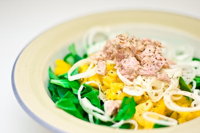 Tuna on top of salad and onions in a plate.