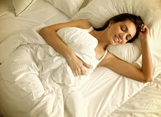 A woman lying in the bed with a smile on her face covered by a white blanket.