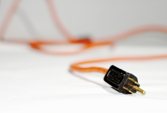 A power cord with an orange wire lying unplugged on a white surface.