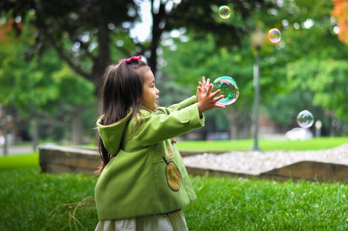 A little girl in a park running after a soap bubble, who is the only kid in her family