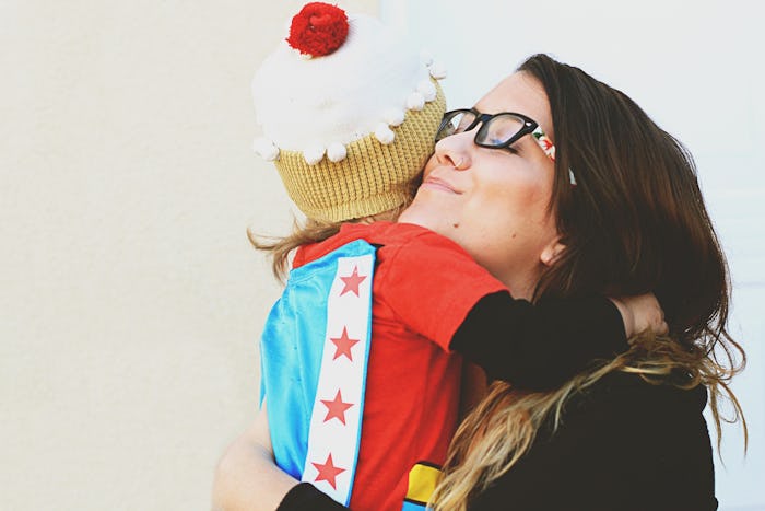 A mother hugging her daughter with a cupcake beanie on her head.