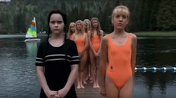 Wednesday adams in a black swimsuit next to girls in orange ones from the movie the adams family