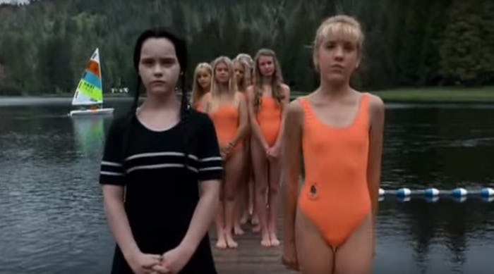 Wednesday adams in a black swimsuit next to girls in orange ones from the movie the adams family.