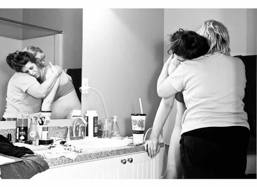 An exhausted pregnant woman is standing in the bathroom while the other woman is hugging her.