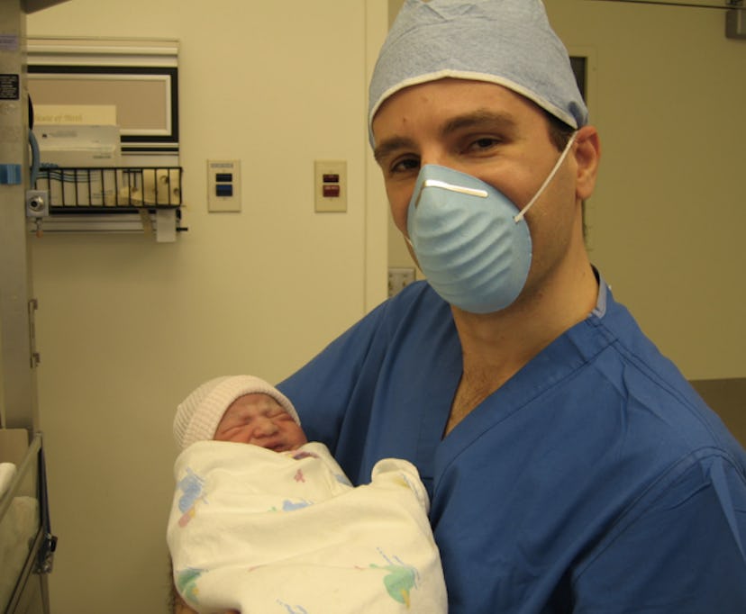 A doctor with a surgical mask on holding a newborn