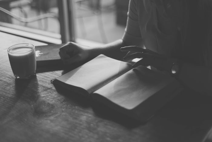 A woman reading a book while sitting at a table with a drink next to her with a black-white color fi...
