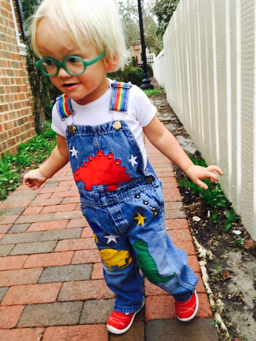 Amos wearing a denim overall with dino patches and green glasses standing outside