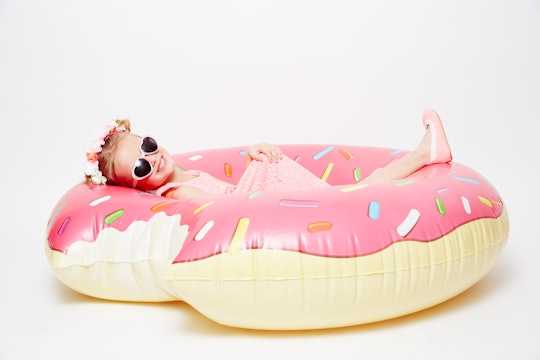 A five year old girl with a floral crown and sunglasses lying on an inflatable pink-white pool donut