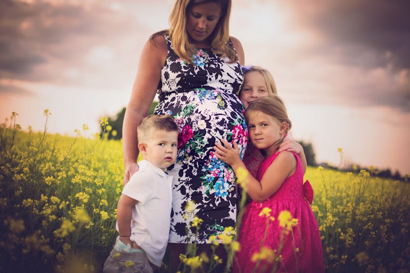 Pregnant Chaunie Brusie being hugged by her three kids while standing in a field of yellow flowers