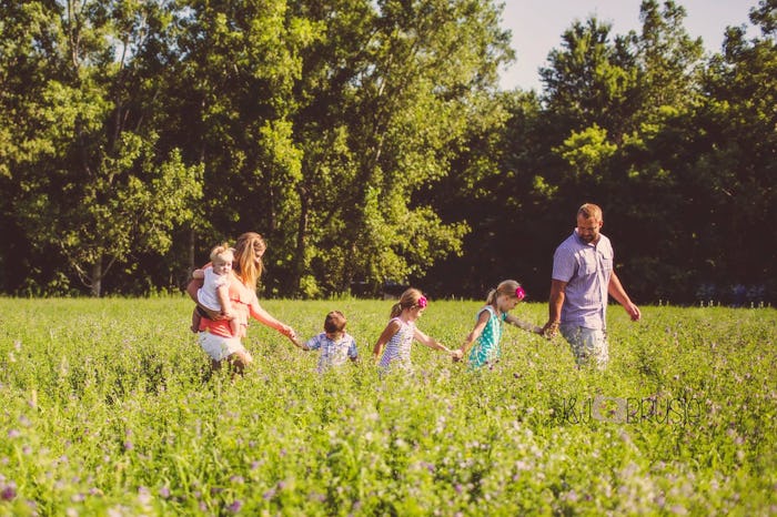 Chaunie Brusie and her husband hold the hands of their three children as they walk through a field
